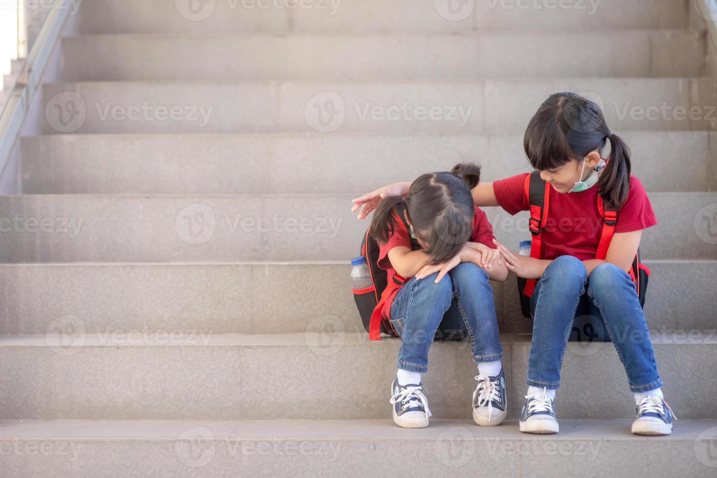 porträtt av skol gråt medan Sammanträde på trappa utomhus med leende syster tröstande henne, kopia Plats foto
