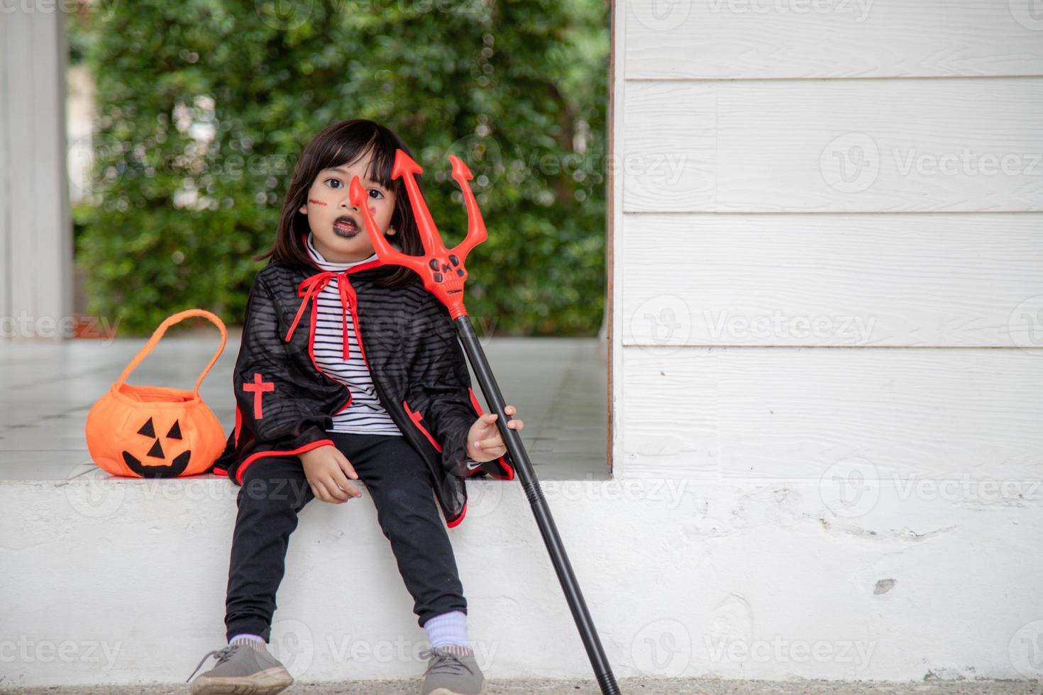 asiatisk barn flicka i demon kostym innehav svart och röd treudd, Lycklig halloween begrepp foto