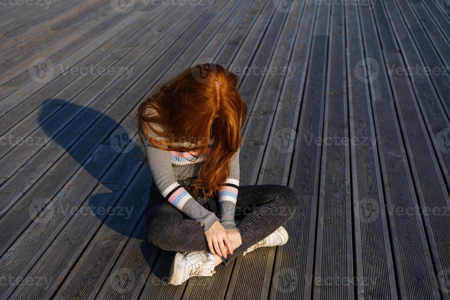 ledsen rödhårig flicka Sammanträde på en trä- bakgrund foto