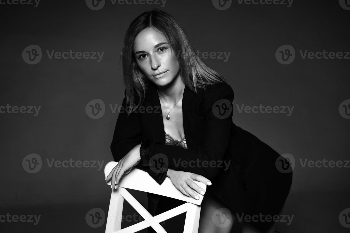 kvinna Framställ Sammanträde på en stol i jacka och underkläder, svart och vit Foto