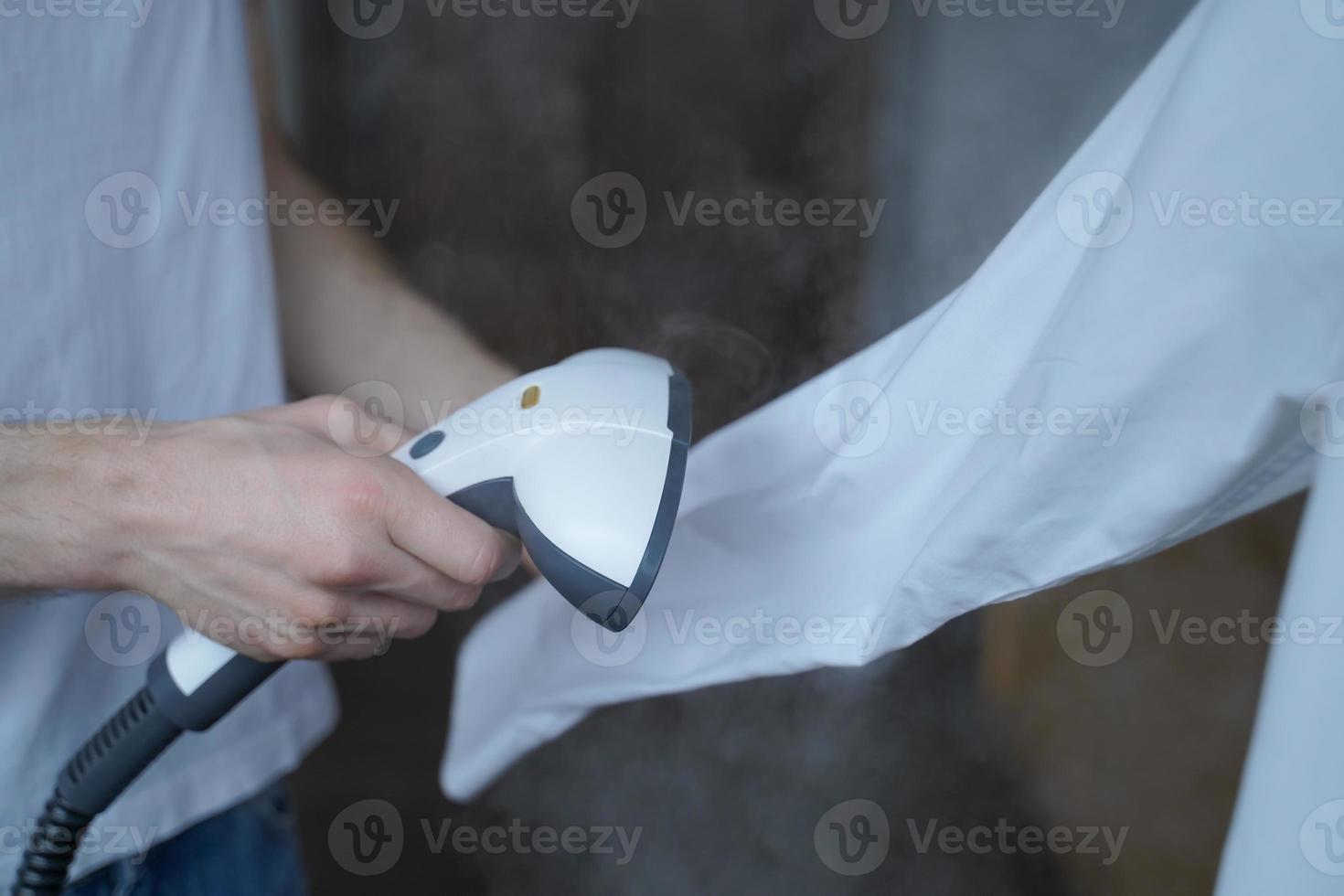 beskuret foto av man som använder ångbåten och stryker prydligt vit skjorta medan han håller långärmad