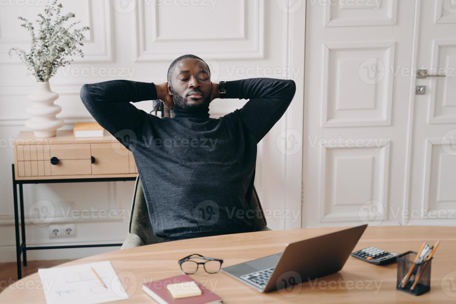 trött överansträngd afroamerikansk manlig kontorsarbetare vilar med slutna ögon och händer bakom huvudet foto