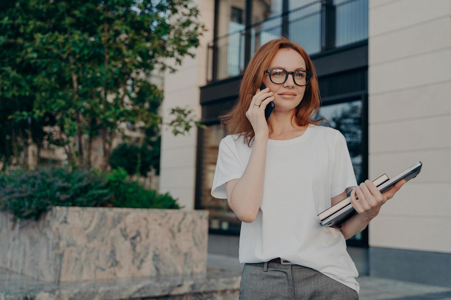 omtänksam rödhårig kvinna tittar på avstånd gör telefonsamtal håller smartphone nära örat foto