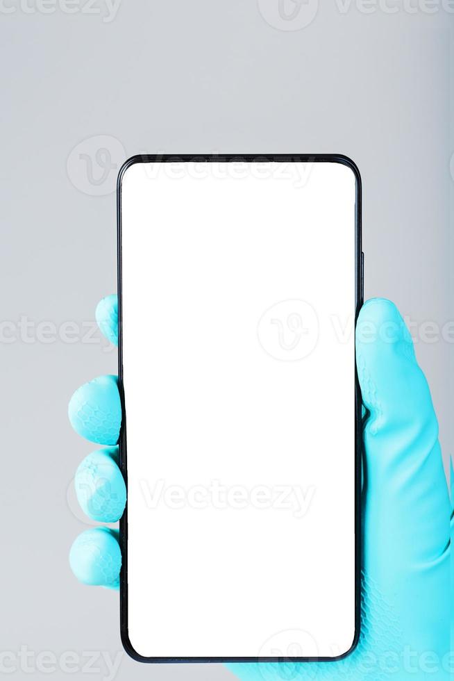 smartphone med en rena vit skärm i de hand i en blå medicinsk handske närbild. foto