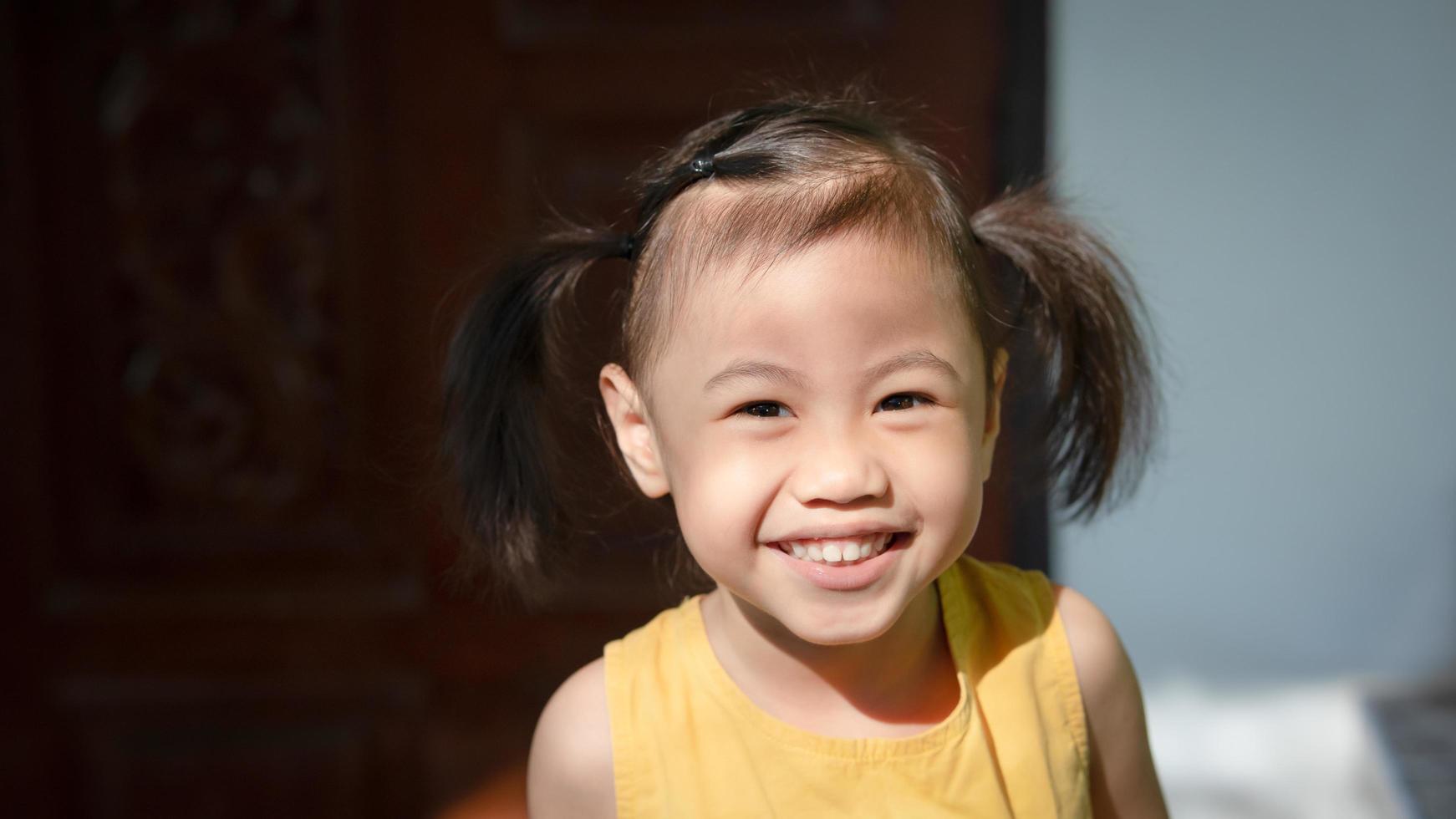 positiv charmig 4 år gammal söt bebis asiatisk flicka, liten preschooler barn leende och ser på kamera. foto