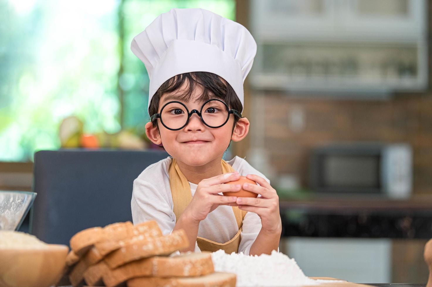 söt liten asiatisk glad pojke intresserad av matlagning foto