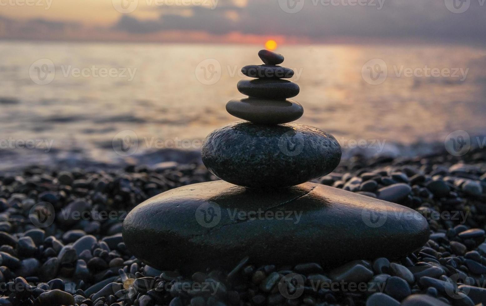 pyramid av sten stenar med Sol på topp mot bakgrund av hav och solnedgång himmel. zen stenar, meditation begrepp foto