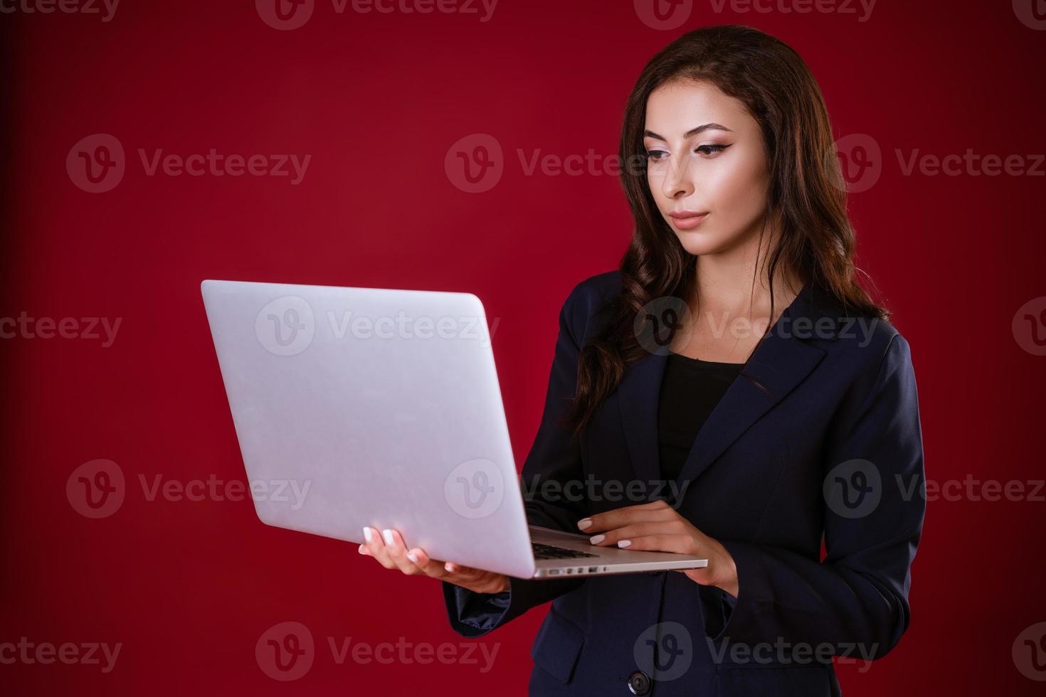 ung kvinna bestämmer företag fall i en bärbar dator på en röd studio bakgrund. foto