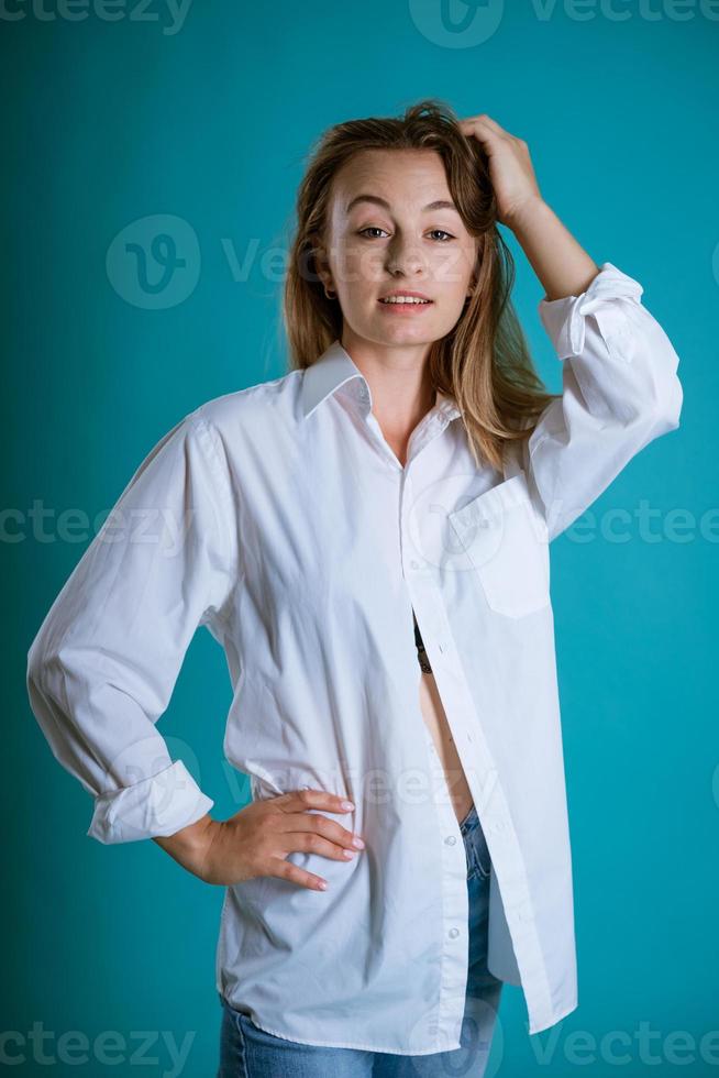 ung kvinna Framställ i vit skjorta och jeans på blå bakgrund foto