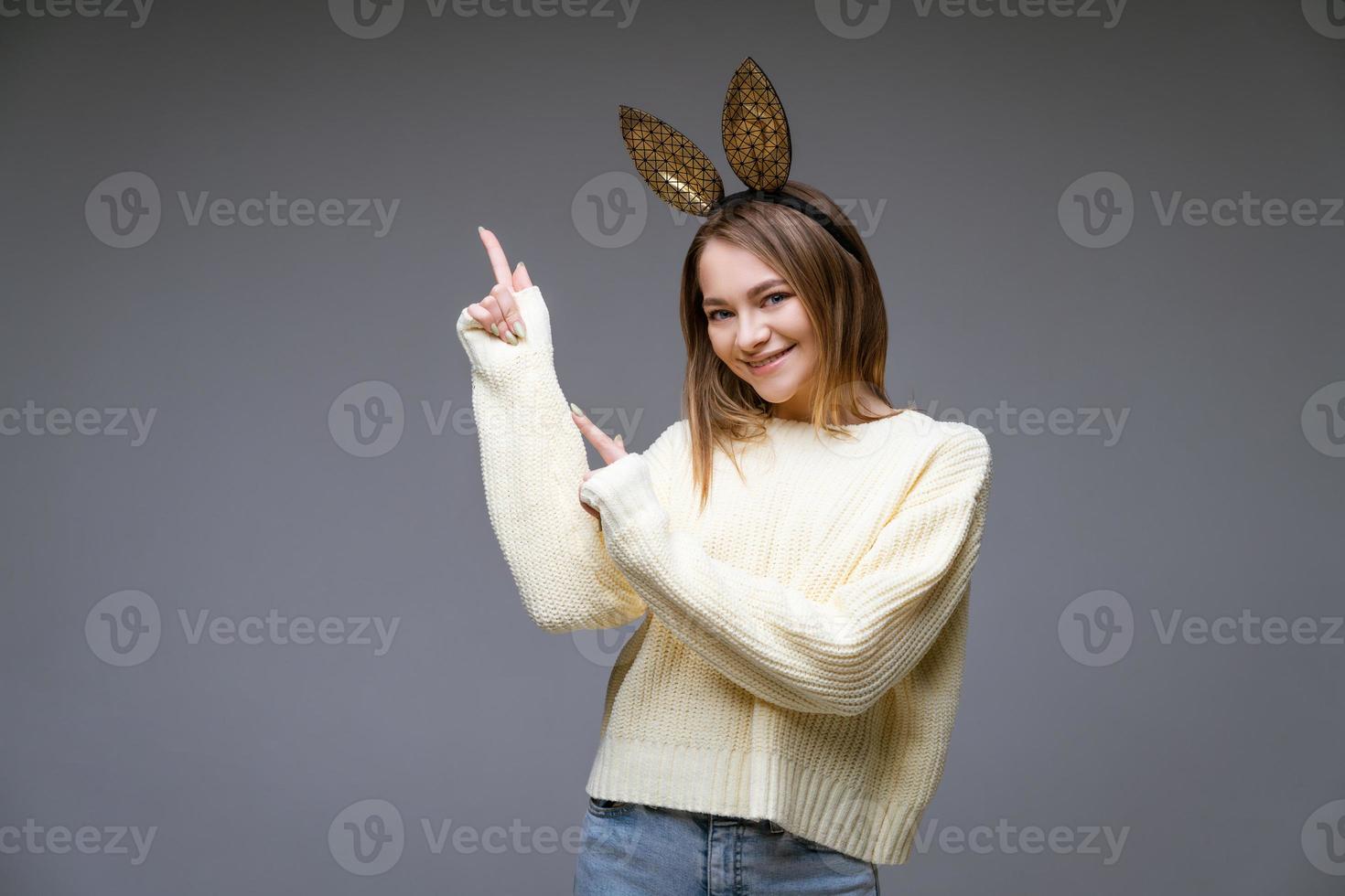 skön ung kvinna i kanin öron visar henne finger till sida på bakgrund foto