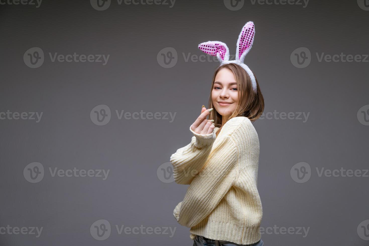 leende ung flicka med kanin öron visar en mini hjärta med fingrar foto