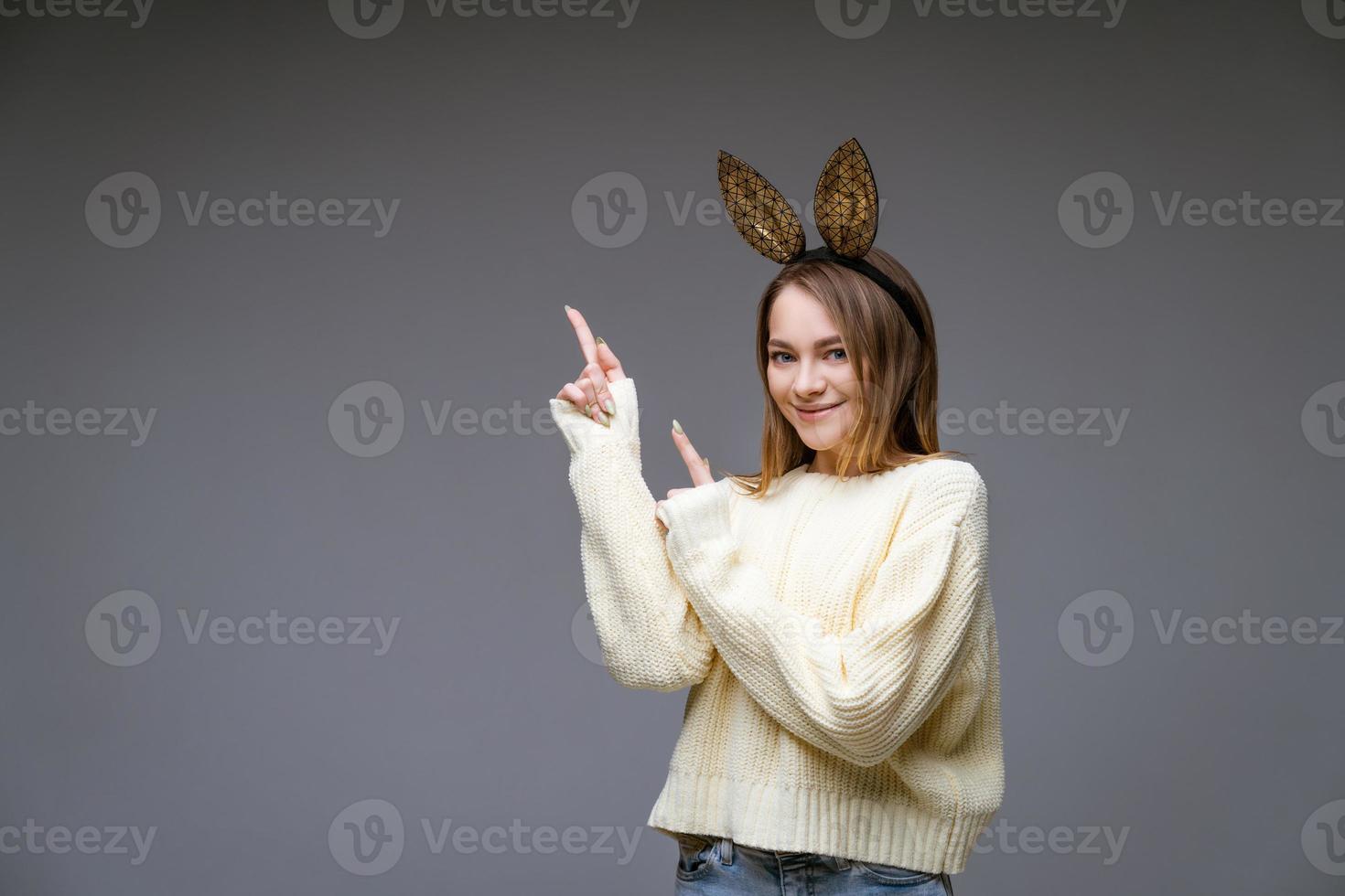 skön ung kvinna i kanin öron visar henne finger till sida på bakgrund foto