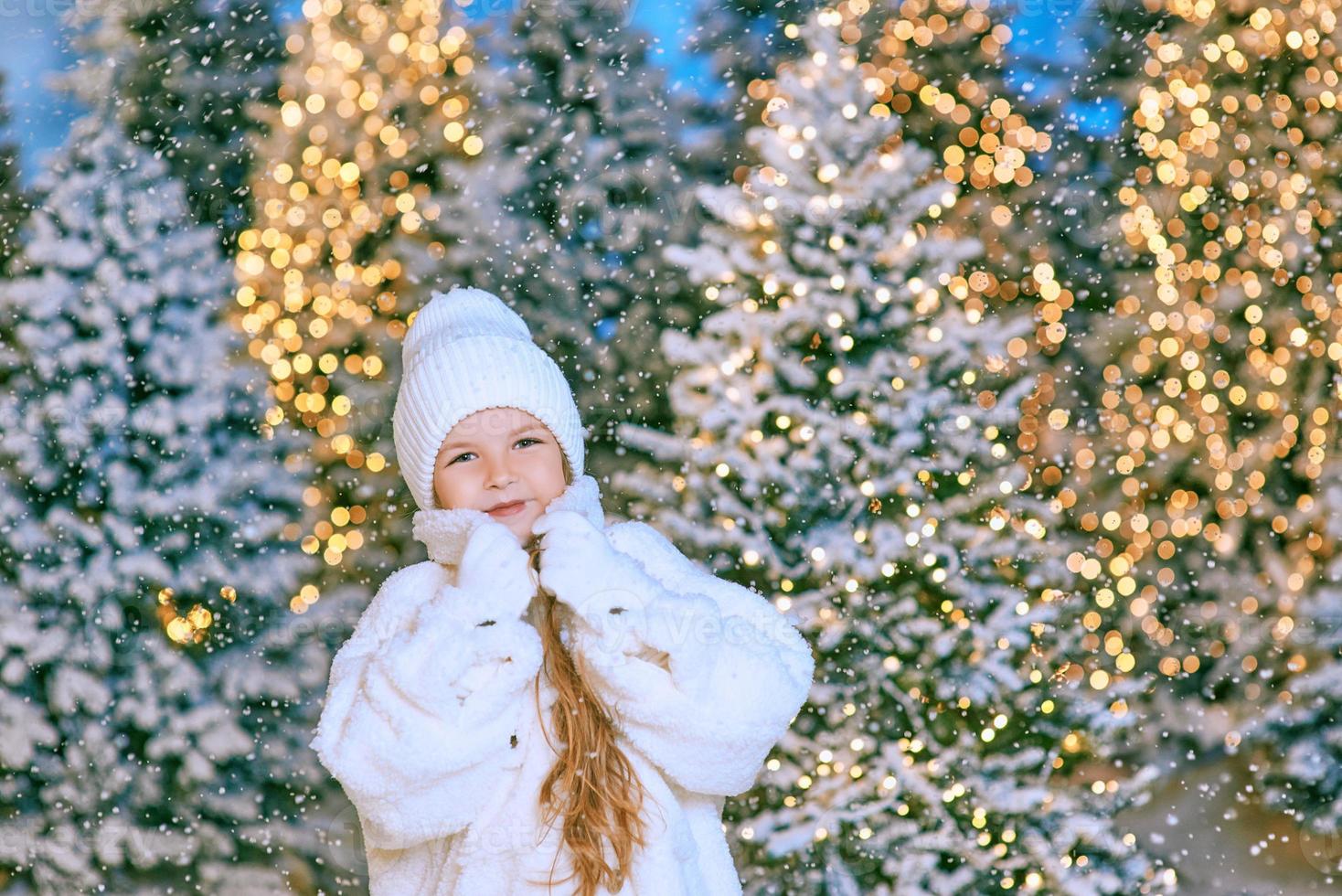 söt kaukasisk blond flicka i vit eko-pälsrock, mössa och handskar som går i vinterjulskogen. nytt år, saga, modekoncept foto