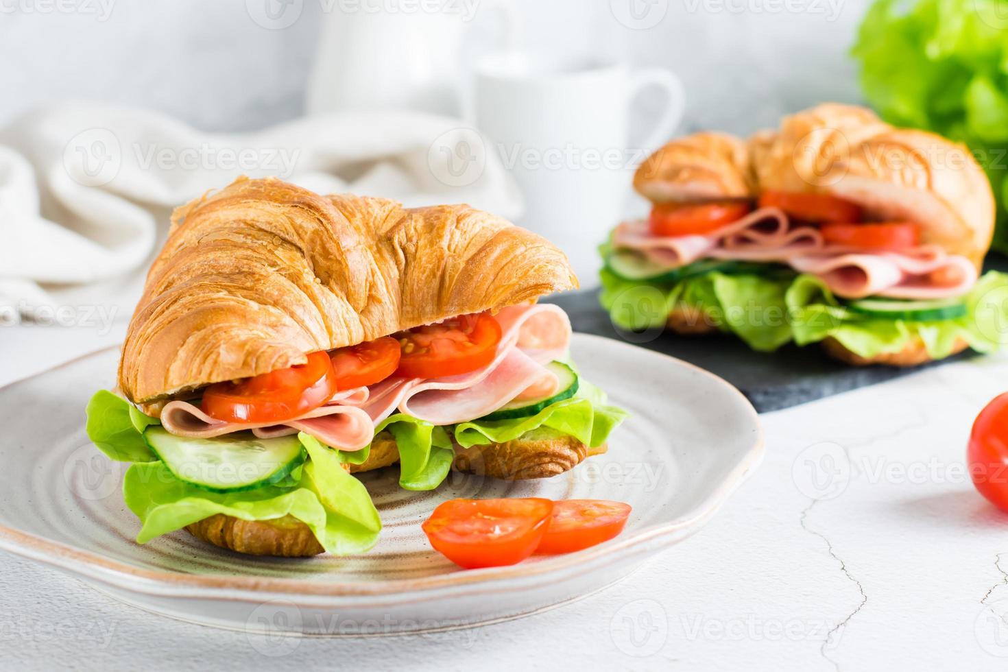 färsk croissant smörgås med skinka, grönsaker och sallad på en tallrik. hemlagad snabb mat. foto