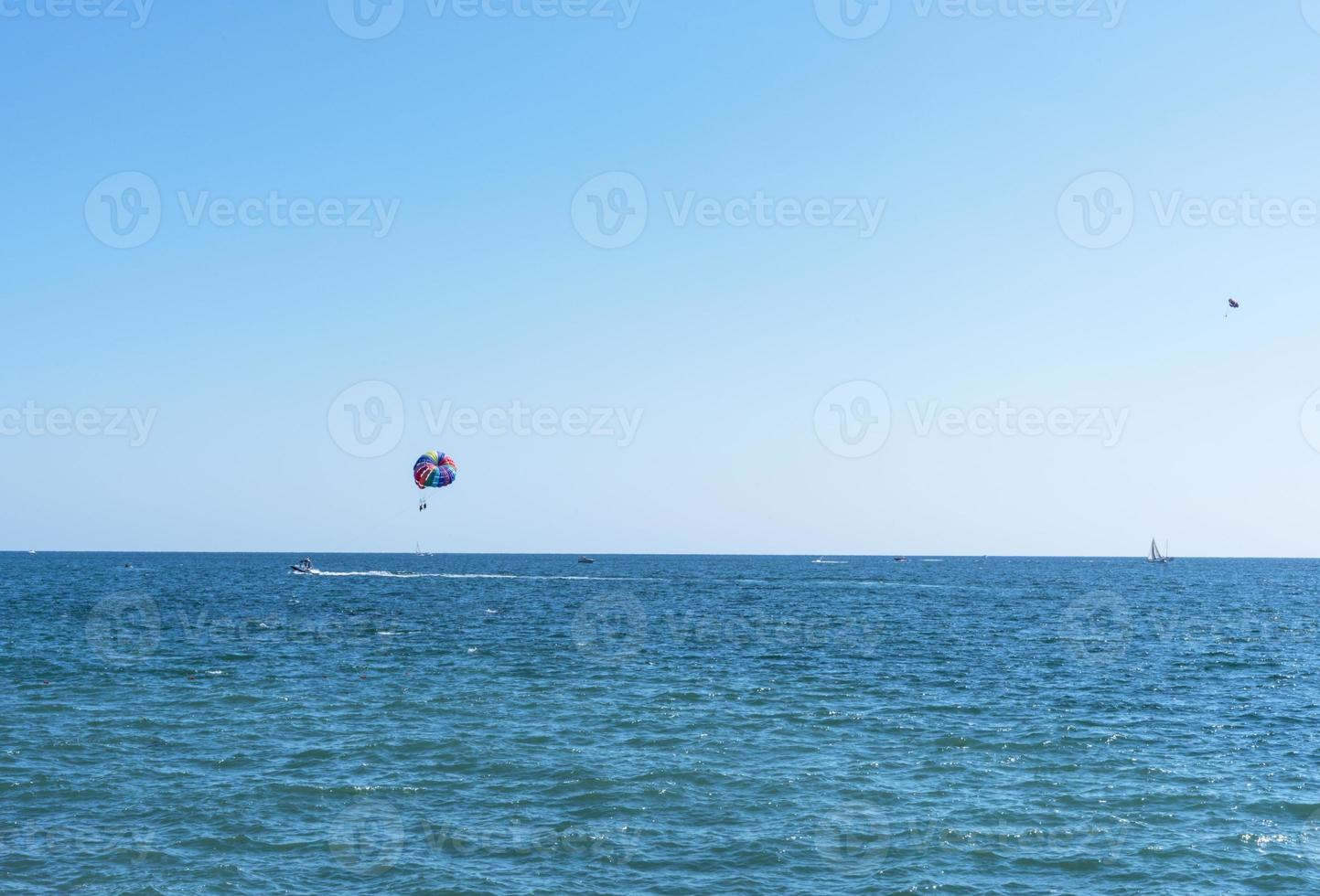 parasailing flerfärgad regnbåge fallskärm Bakom båt över blå turkos hav landskap sommar aktiviteter kopia Plats selektiv fokus foto