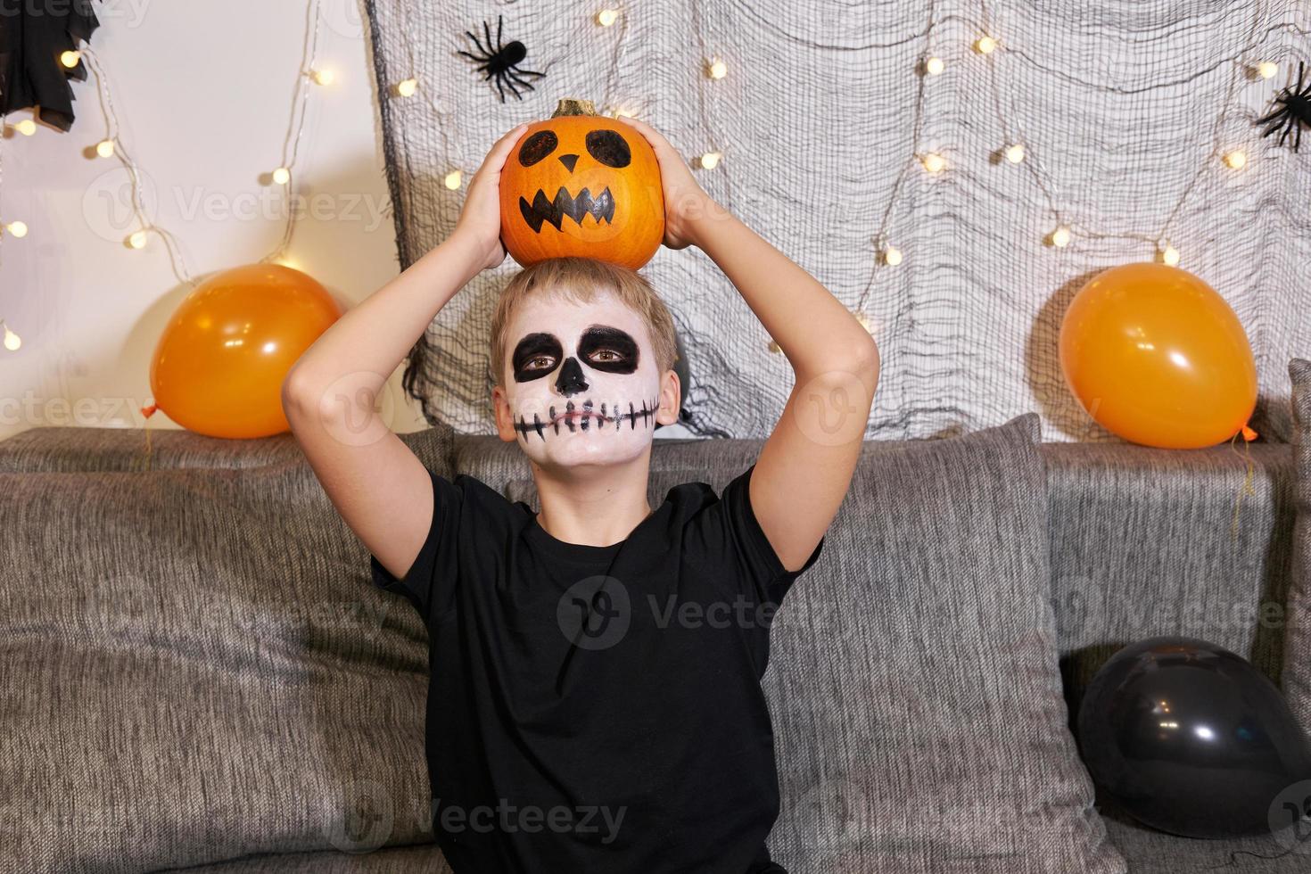 tonåring med smink på hans ansikte och med en pumpa i hans händer för halloween. foto