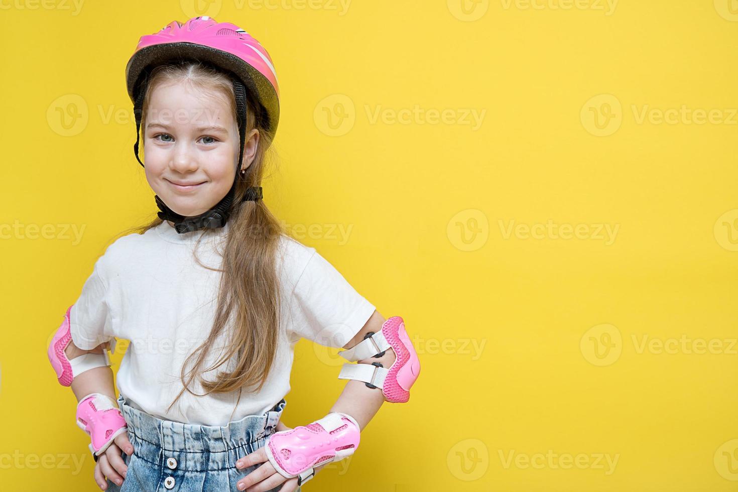 liten söt flicka i skydd för vält skridskoåkning eller cykling står på en gul bakgrund med henne händer på henne bälte och ler, de begrepp av skydda din barn foto