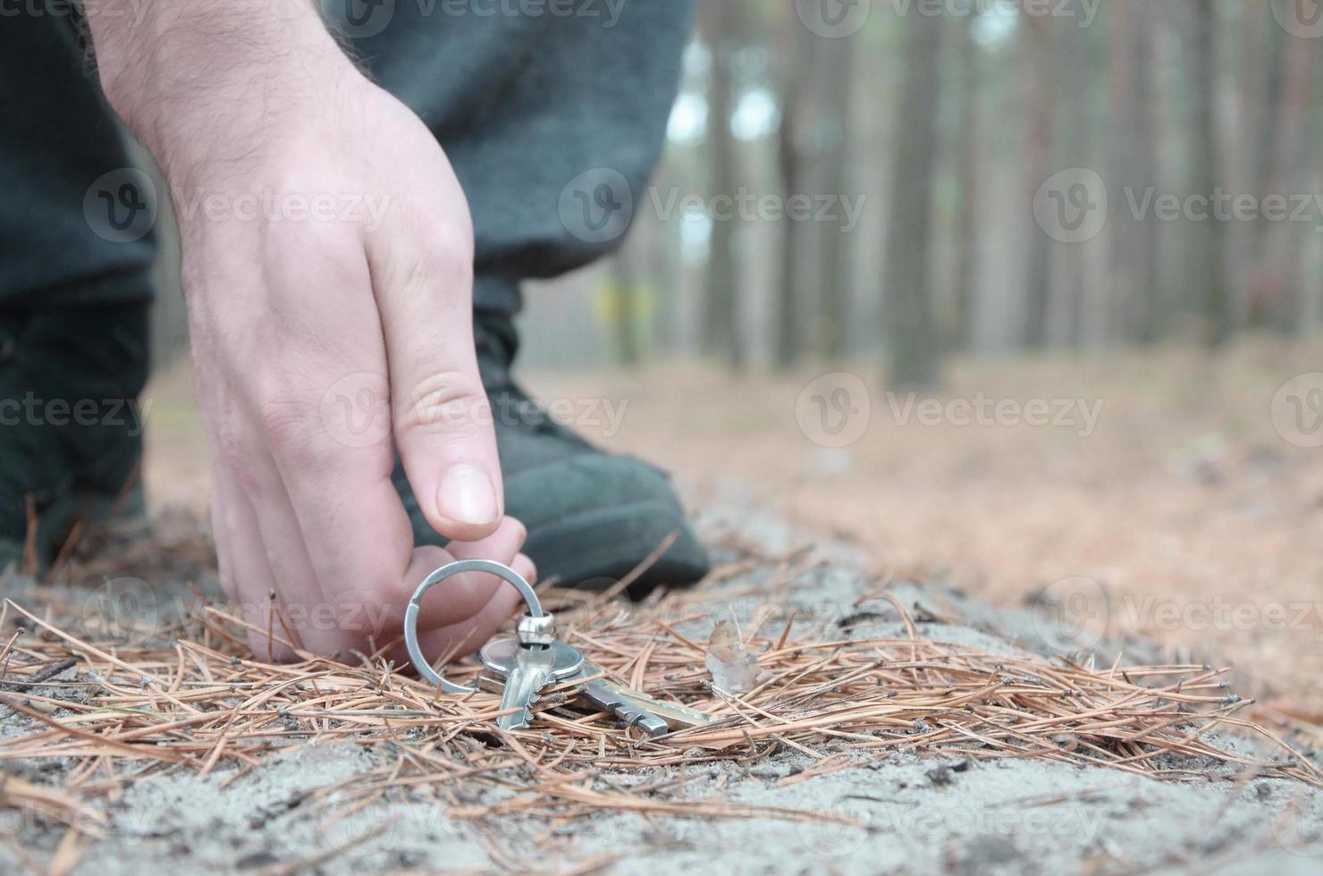 manlig hand plockning upp förlorat nycklar från en jord i höst gran trä väg. de begrepp av upptäckt en värdefullt sak och Bra tur foto