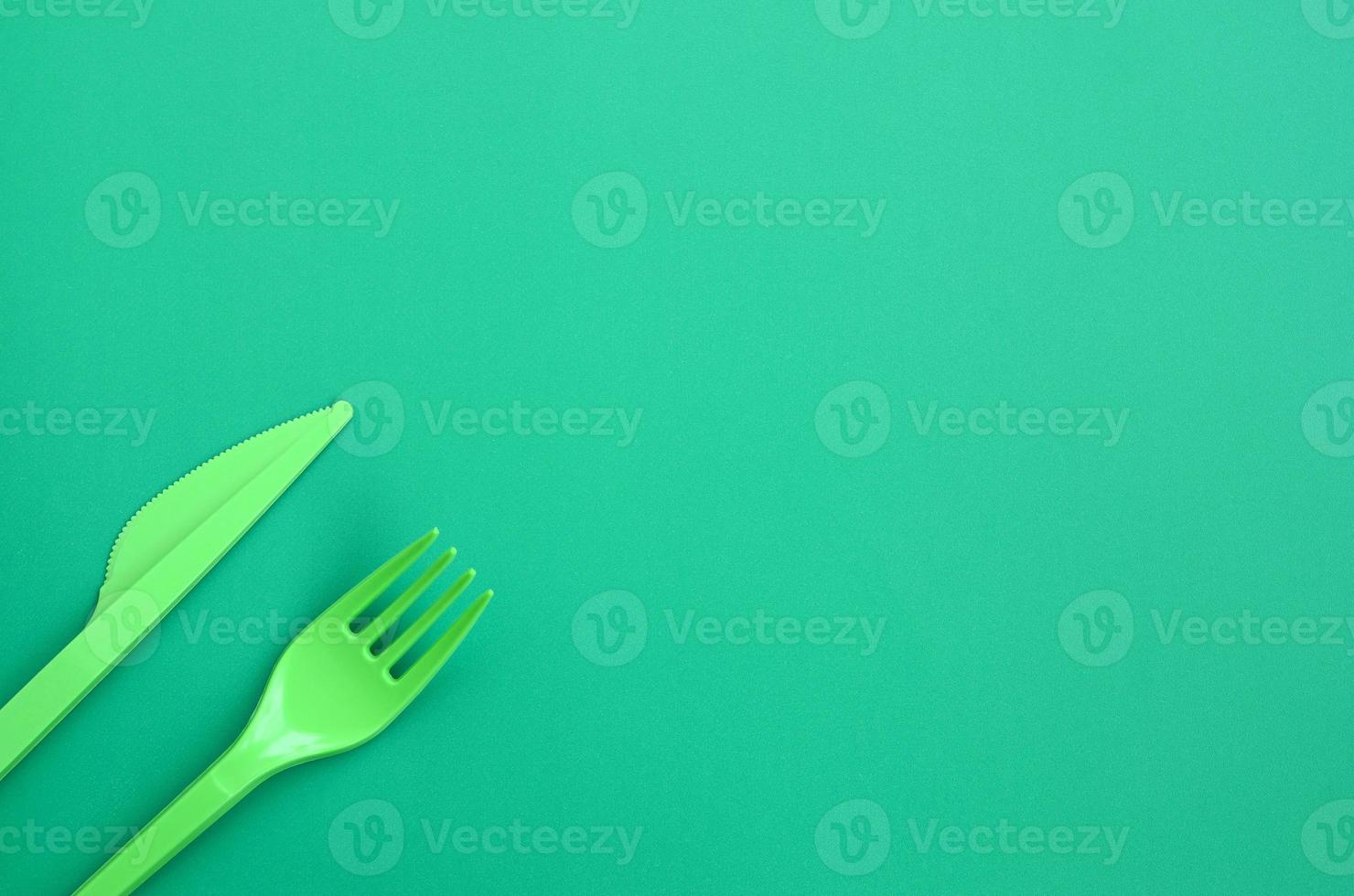 disponibel plast bestick grön. plast gaffel och kniv lögn på en grön bakgrund yta foto