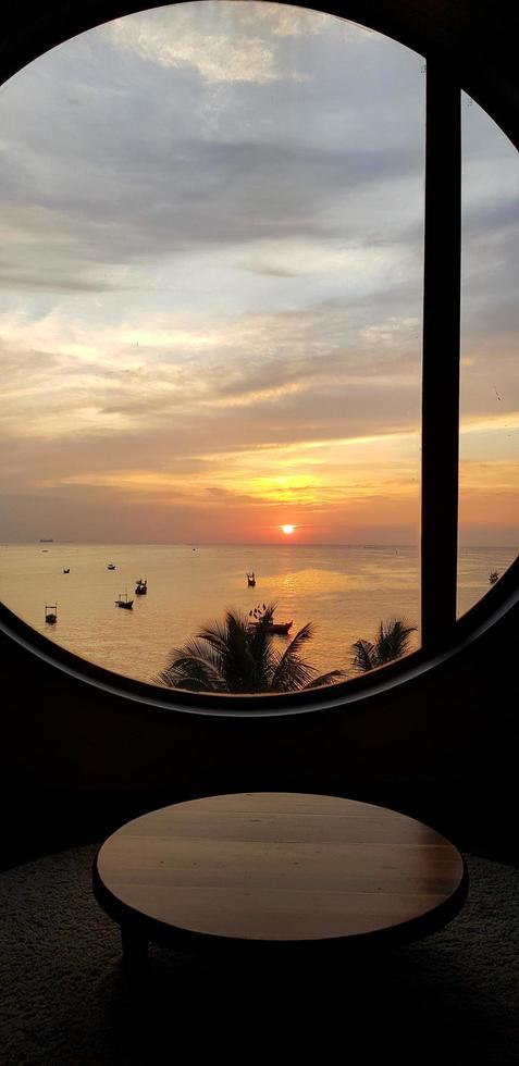 silhuett av tabell och fönster med hav, himmel, kokos träd och solnedgång eller soluppgång bakgrund på bangsaen strand chonburi, thailand. marinmålning med solljus och landskap se foto