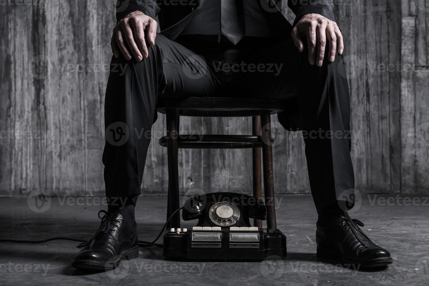 väntar för Viktig ringa upp. närbild av bossig man i formell klädsel Sammanträde på de stol med gammaldags telefon om nära hans fötter foto