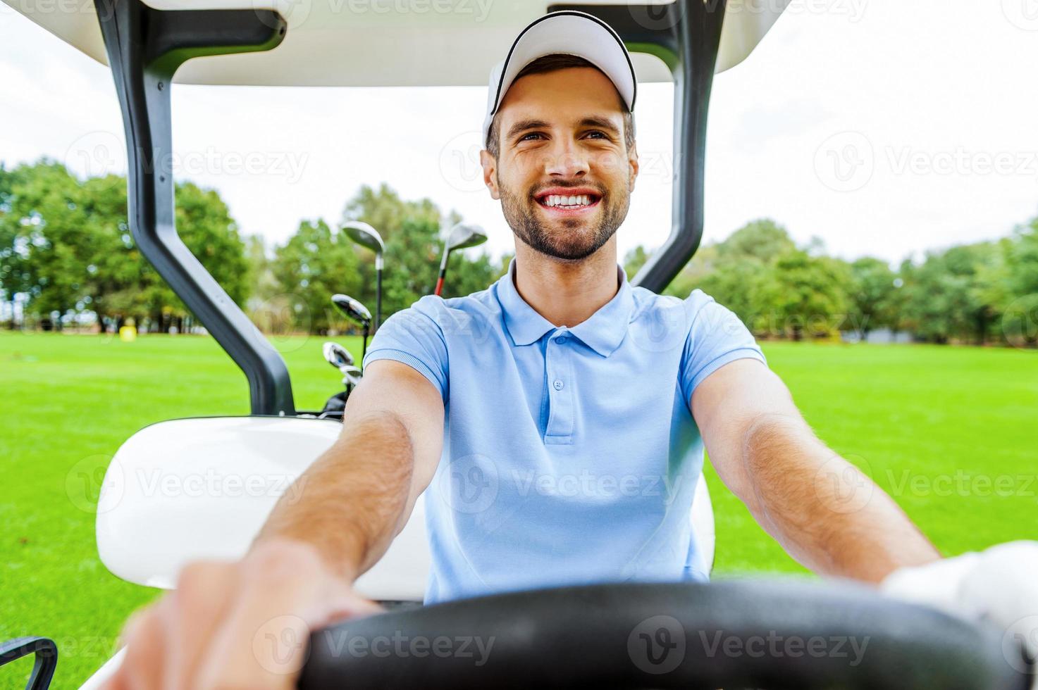 körning en golf vagn. stilig ung man körning en golf vagn och ser bort foto