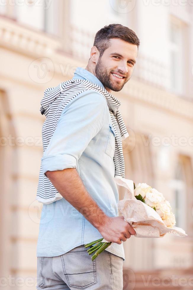 ro för henne. bak- se av glad ung man innehav bukett av blommor och ser över axel medan gående förbi de gata foto