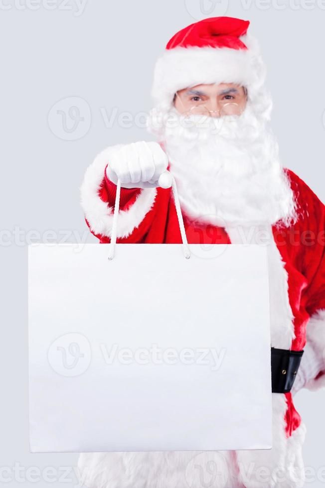 detta är för du traditionell santa claus stretching ut hand med handla väska medan stående mot grå bakgrund foto