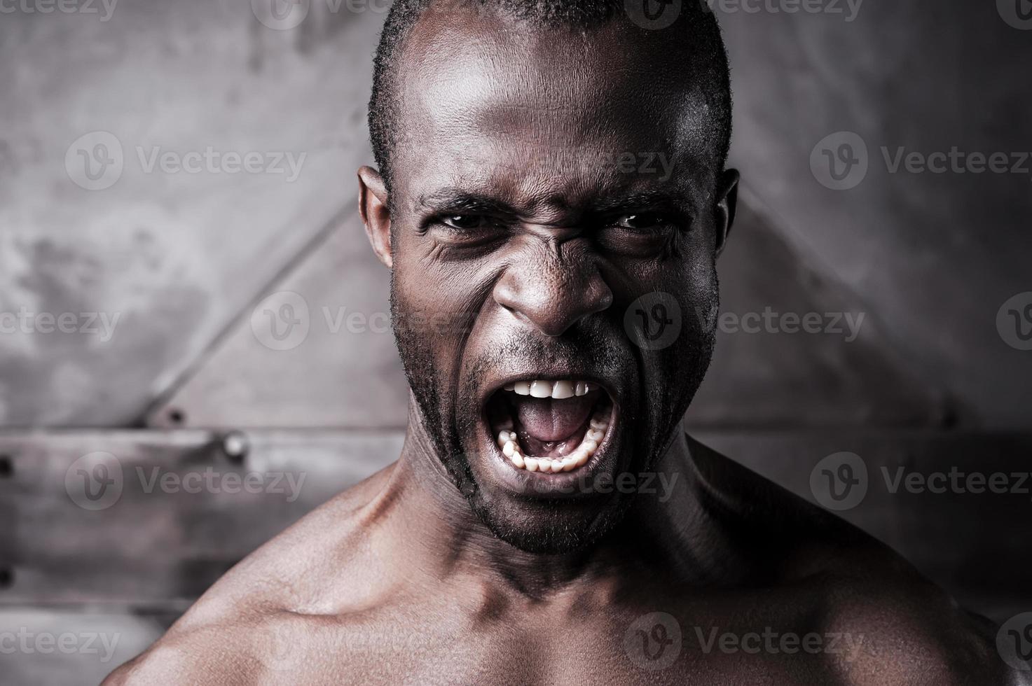 rasande och aggressiv. porträtt av rasande ung bar överkropp afrikansk man skrikande och ser på kamera foto
