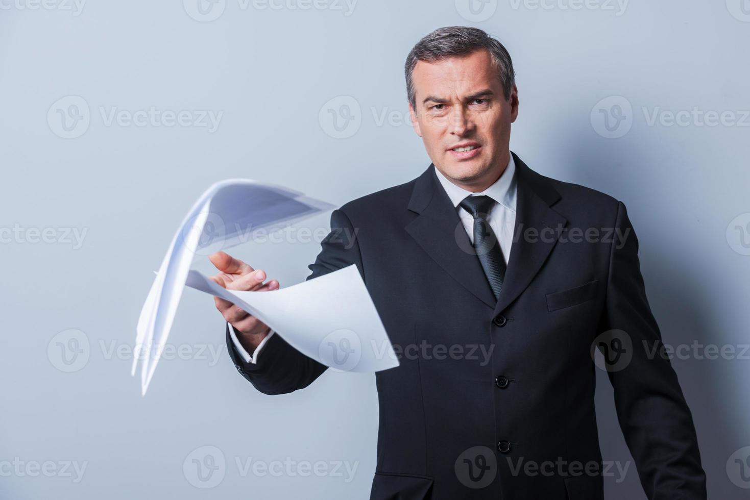 den där är Allt fel rasande mogna man i formell klädsel kasta dokument medan stående mot grå bakgrund foto