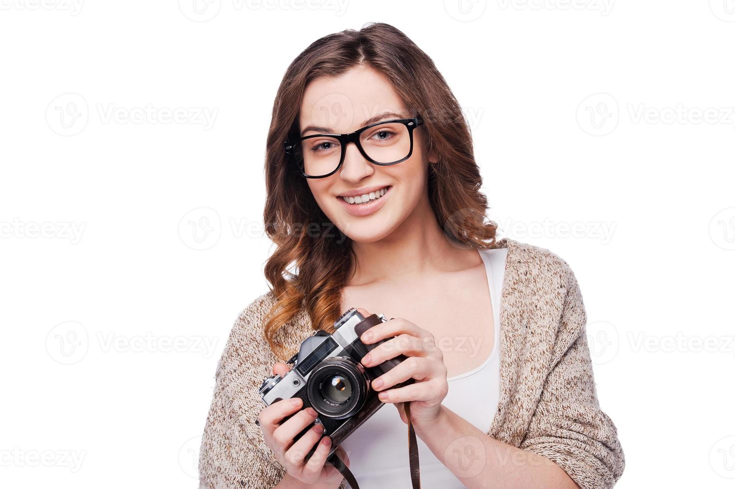 skön fotograf. attraktiv ung leende kvinna innehav kamera medan stående isolerat på vit foto