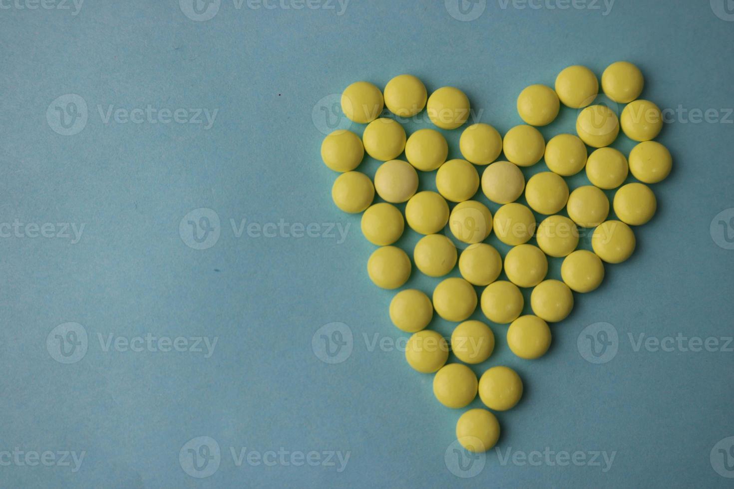 små medicinsk läkemedel runda gul biljard, vitaminer, läkemedel, antibiotika i de form av en hjärta på en blå bakgrund, textur. begrepp medicin, hälsa vård, hjärta sjukdom. platt lägga, topp se foto