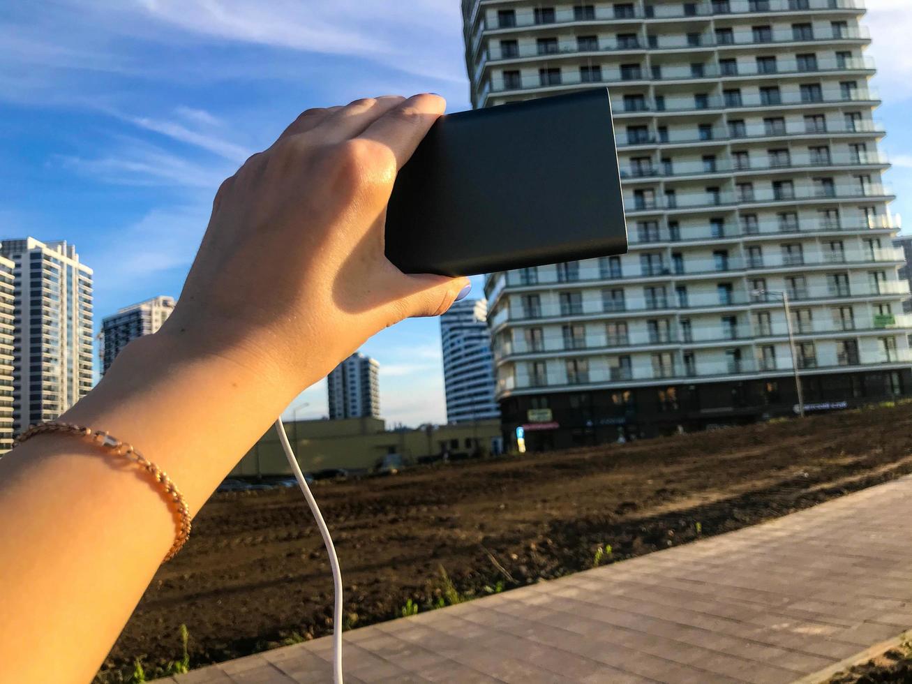 flicka innehav en laddning blockera på de bakgrund av en flera våningar bostads- byggnad. hon är bär en guld mode armband. de byggnad är tillverkad i de arab stil, brun bas av de ingångar foto