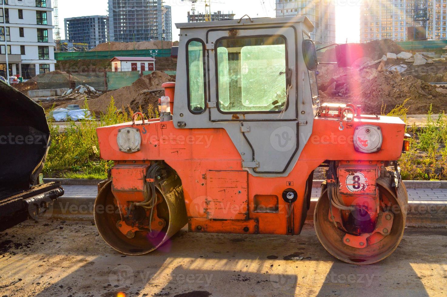 orange ljus asfalt utläggare med stor hjul. metall grå tak, Nästa till de fönster. mot de bakgrund av de brännhet ljus Sol. Avancerad beläggning maskin foto