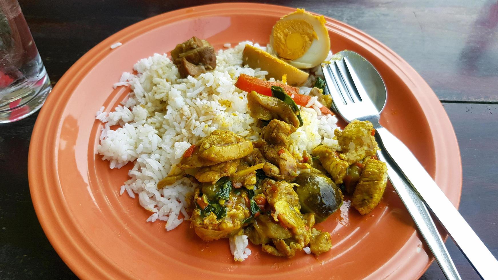 thai mat med kryddad kyckling gul curry, brinjal och stuvad ägg på vit ris med gaffel och sked på orange maträtt eller tallrik på lokal- gata mat. frukost eller lunch för människor i thailand äta. foto