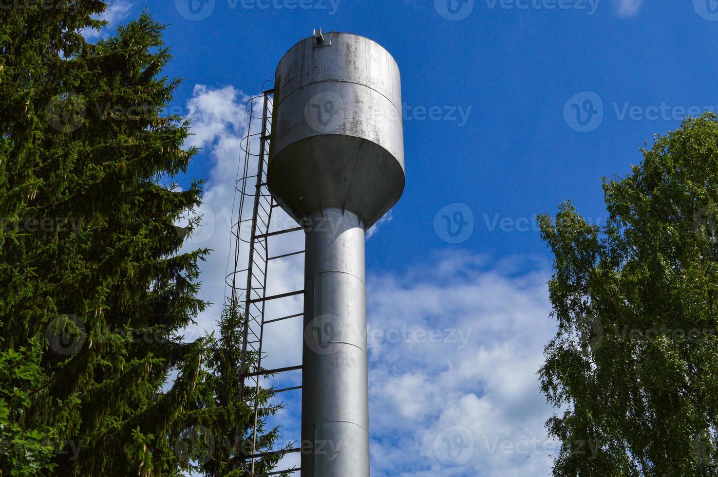 stor järn metall skinande rostfri industriell vatten torn för levererar vatten med en stor kapacitet, tunna mot de blå himmel och träd foto
