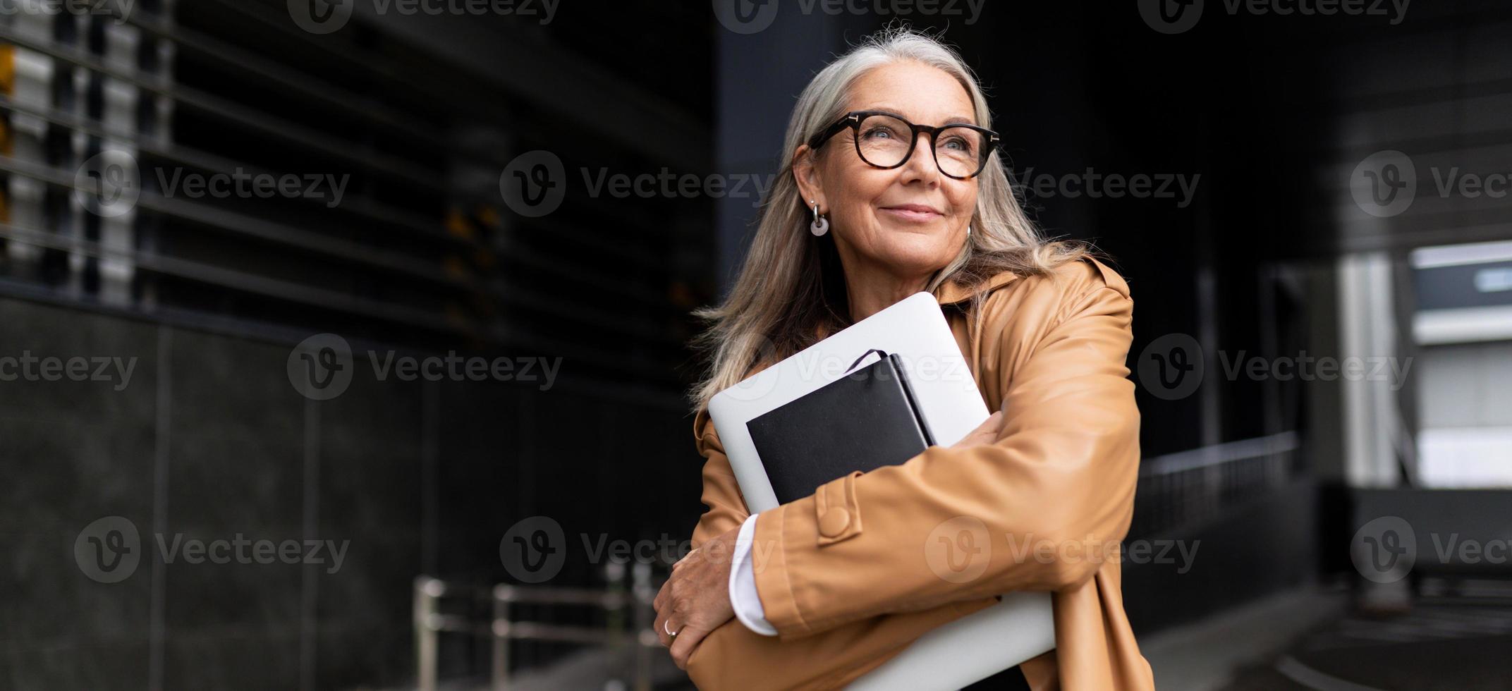 porträtt av ett äldre affärskvinna med en bärbar dator i glasögon utanför de kontor, stark och oberoende kvinna begrepp foto