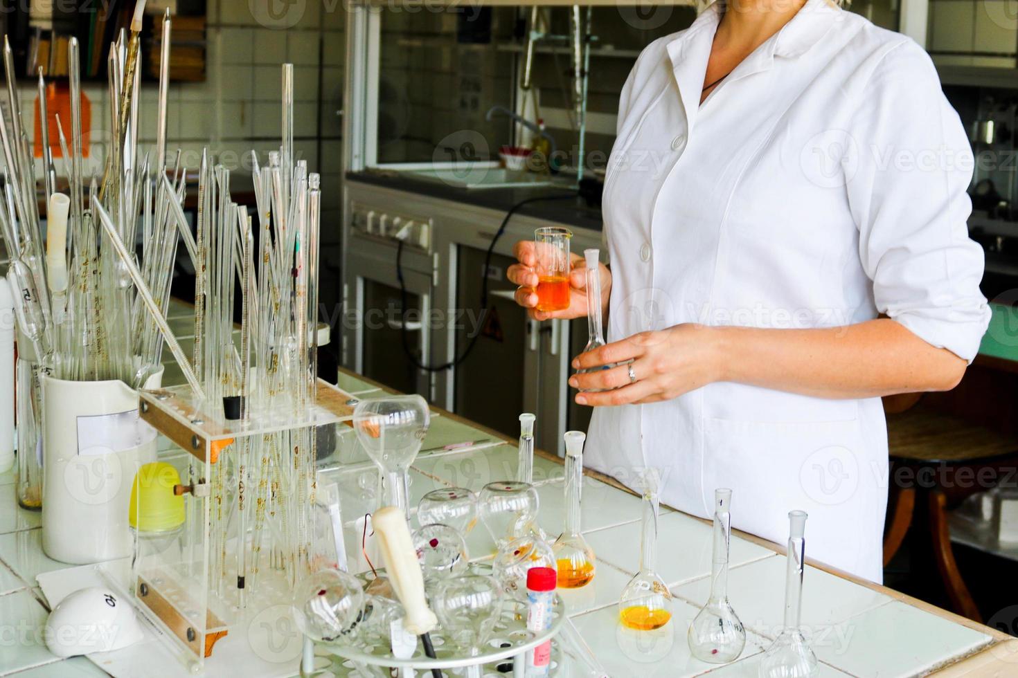 en kvinna laboratorium assistent, en läkare, en kemist, Arbetar med flaskor, testa rör, gör lösningar, mediciner, blandar de Ingredienser i de laboratorium. laboratorium assistent bär ut de forskning foto