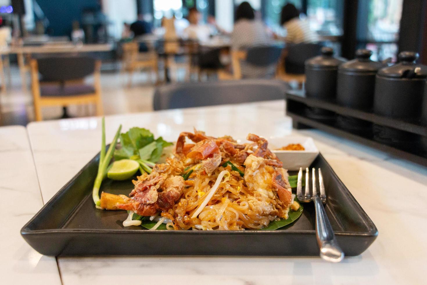Krispig krabbor vaddera thai i svart tallrik på vit tabell i restaurang foto