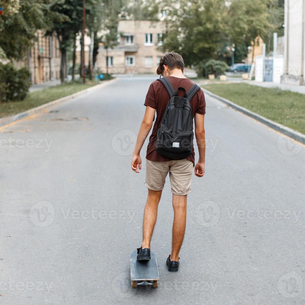 ung stilig kille med en ryggsäck ridning en skateboard på de väg foto