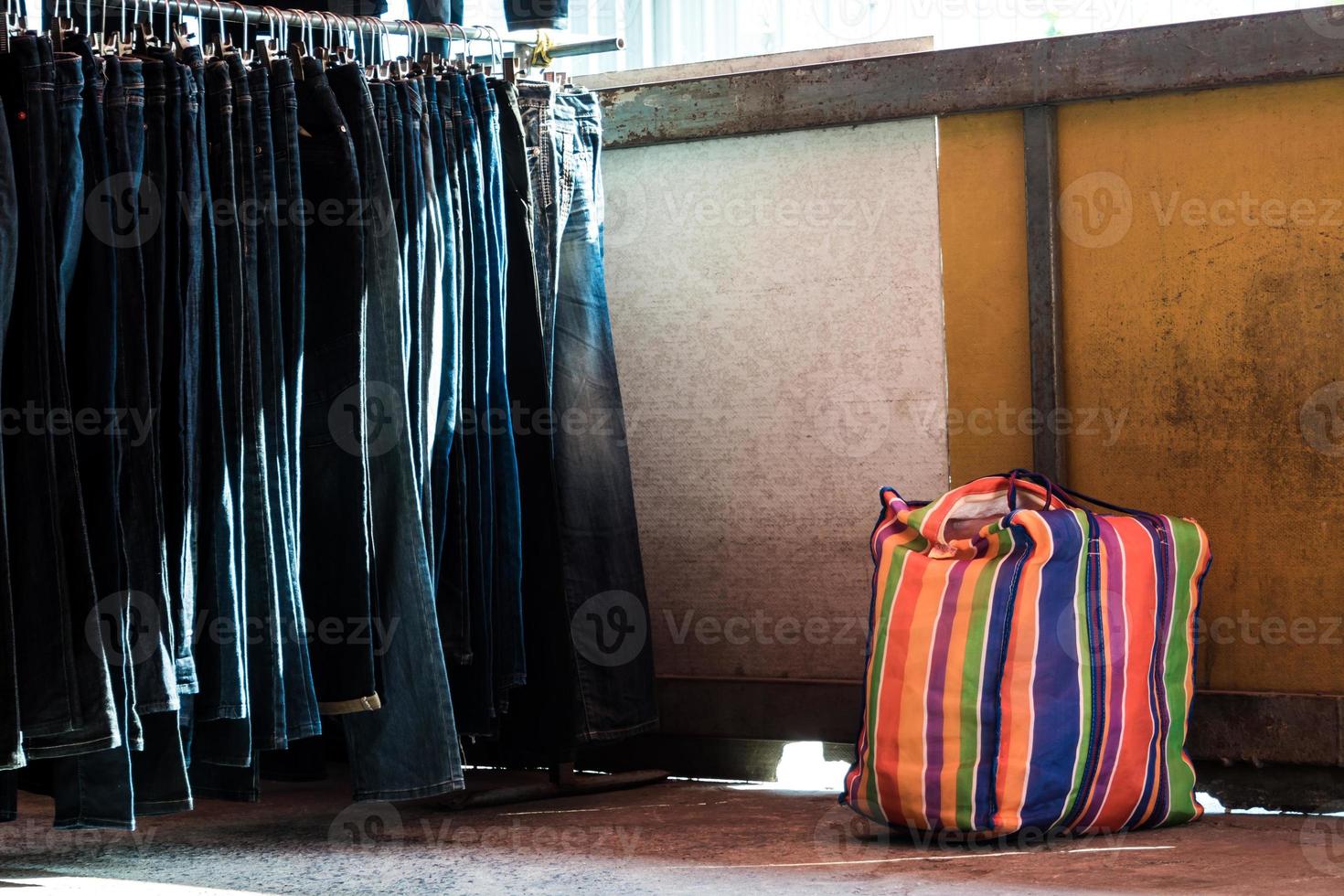 mång Färg på plast säck och de rad av denim byxor hängande på trempels av loppa marknadsföra foto