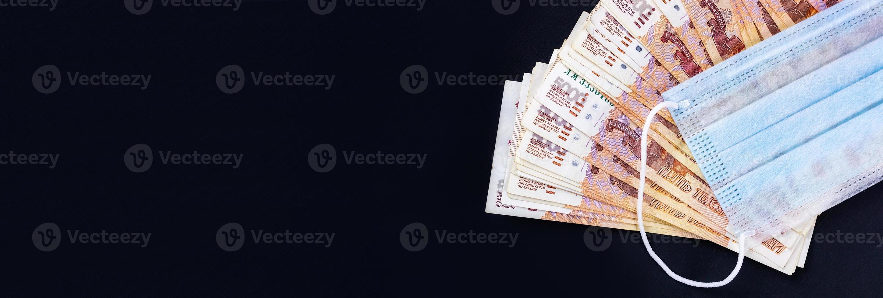 pengar och medicinsk mask på en svart bakgrund foto
