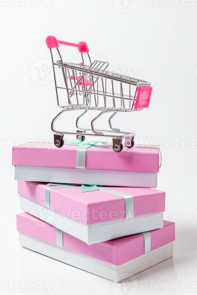 små mataffär matvaror skjuta på vagn för handla leksak med rosa gåva låda isolerat på vit bakgrund. försäljning köpa köpcenter marknadsföra affär konsument begrepp. kopia Plats. foto
