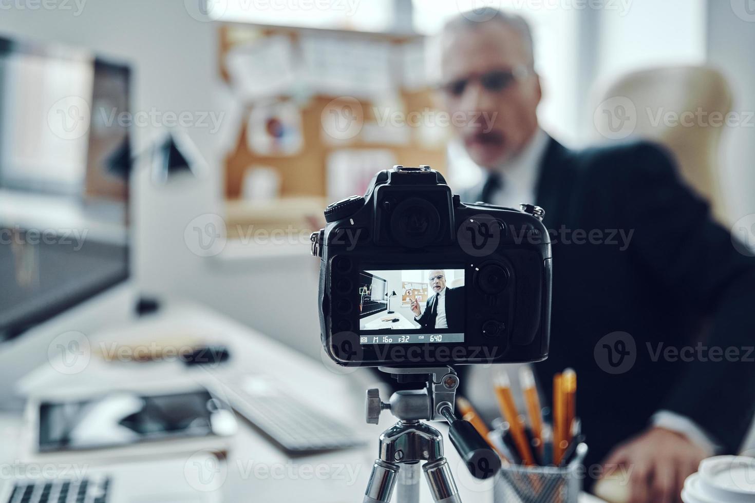 senior man i elegant företag kostym använder sig av modern teknik medan framställning social media video foto