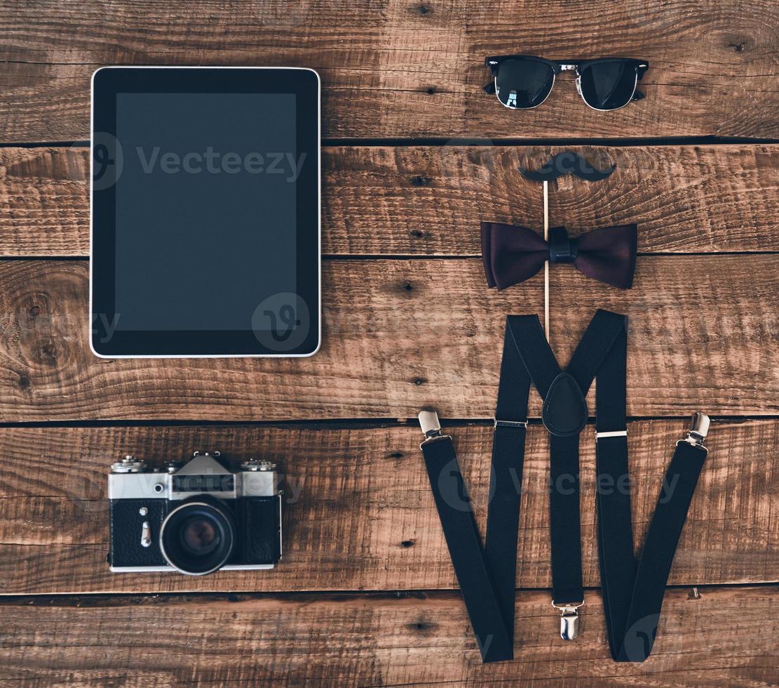modern elegans. hög vinkel skott av digital läsplatta, Foto kamera, hängslen, stötta, rosett slips och glasögon liggande på trä- skrivbord