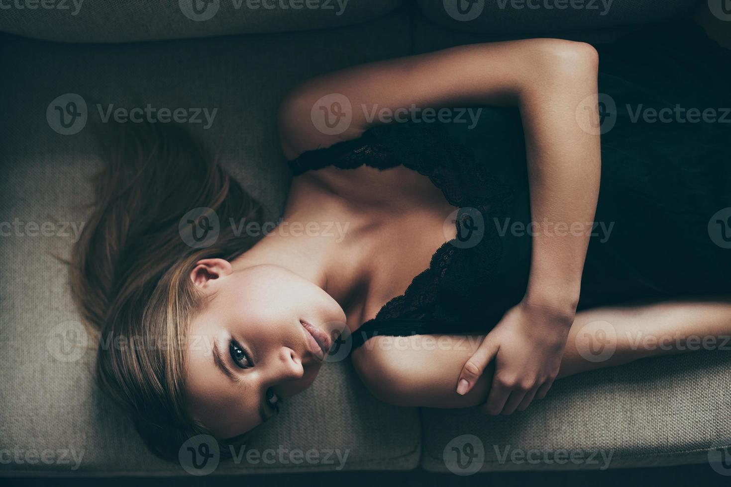 underbar förförerska. topp se av skön ung kvinna i svart underkläder ser på kamera medan liggande på de soffa på Hem foto