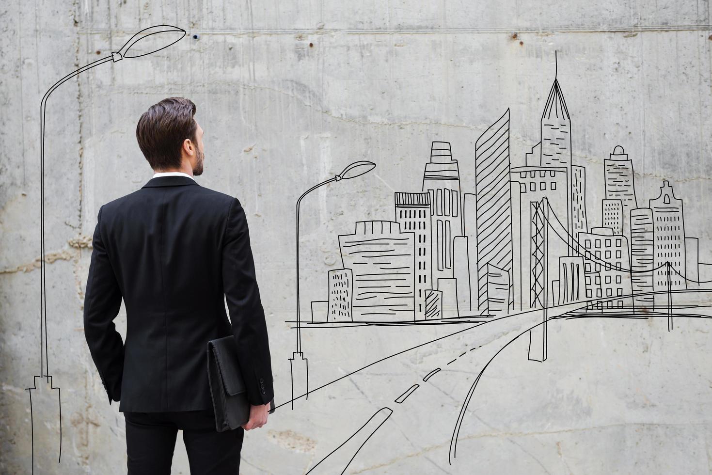 rör på sig fram. bak- se av ung affärsman stående mot betong vägg med stad skiss på den foto