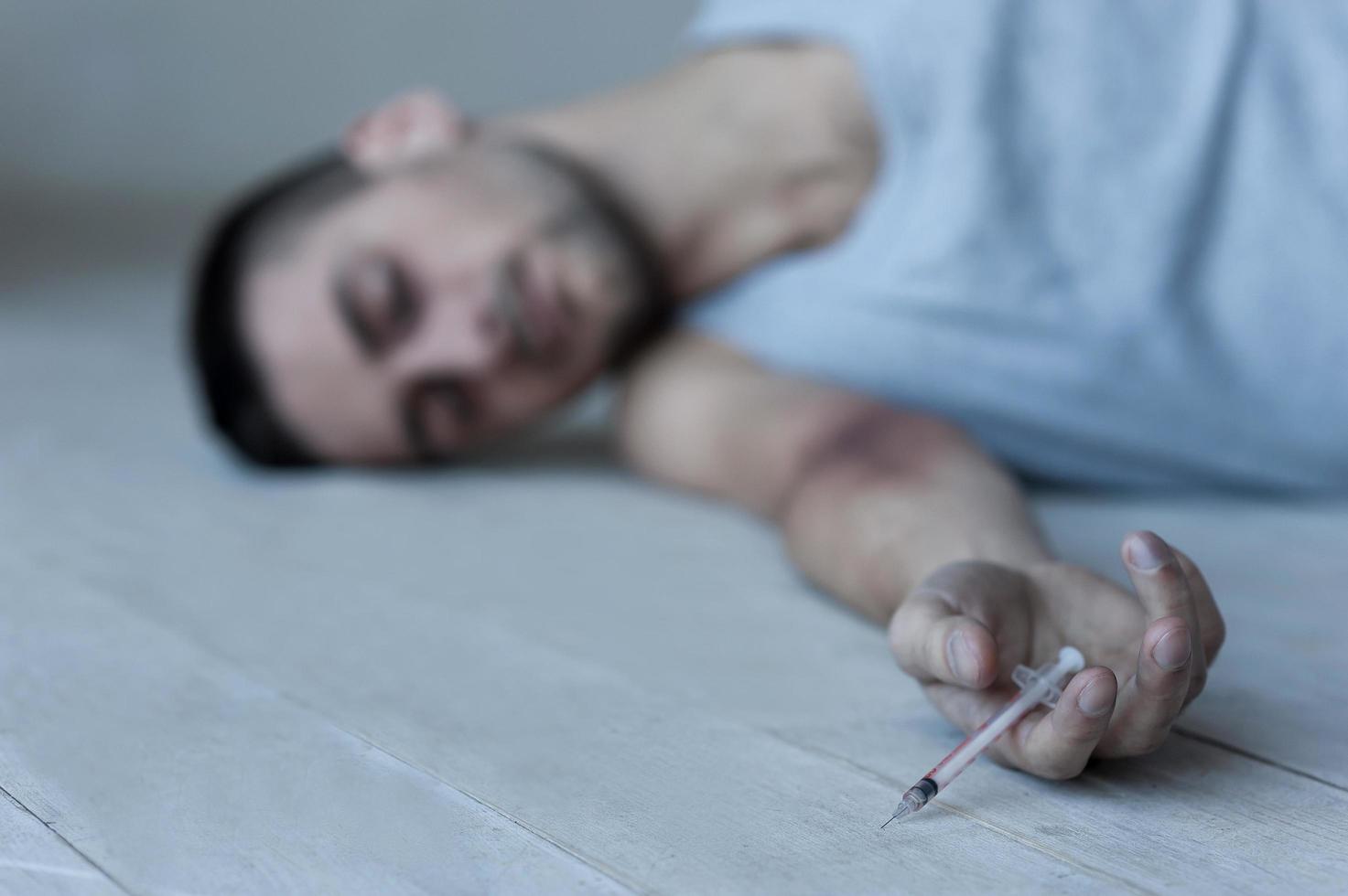 de sista injektion. ung man liggande på de golv och förvaring ögon stängd medan innehav spruta i hans hand foto