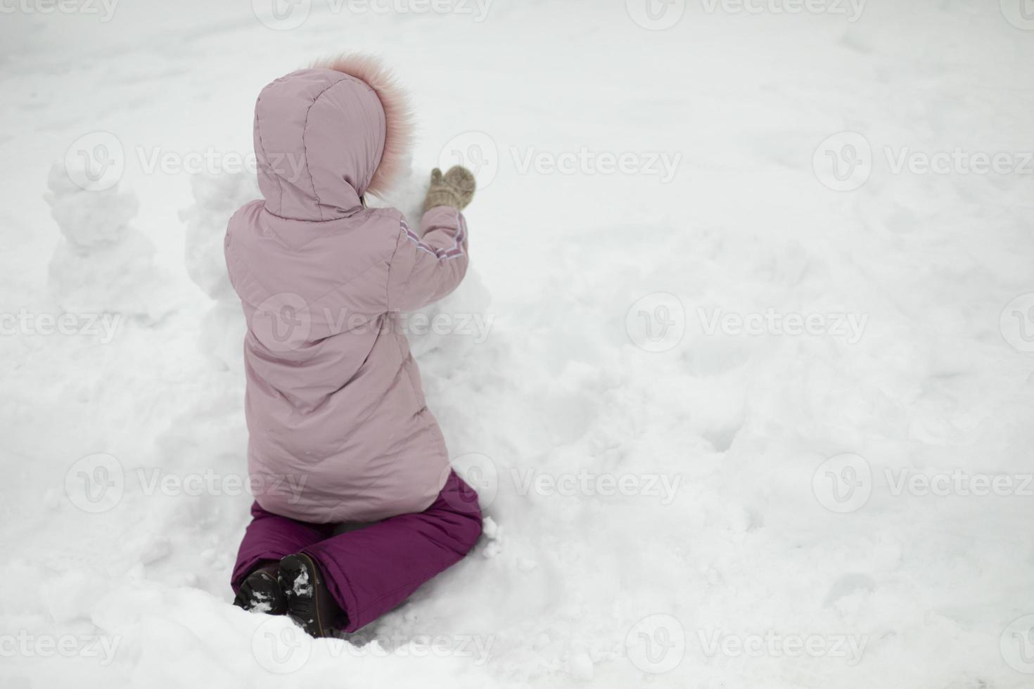 barn leker i snö. flicka på vintern. varma kläder på barnet. foto