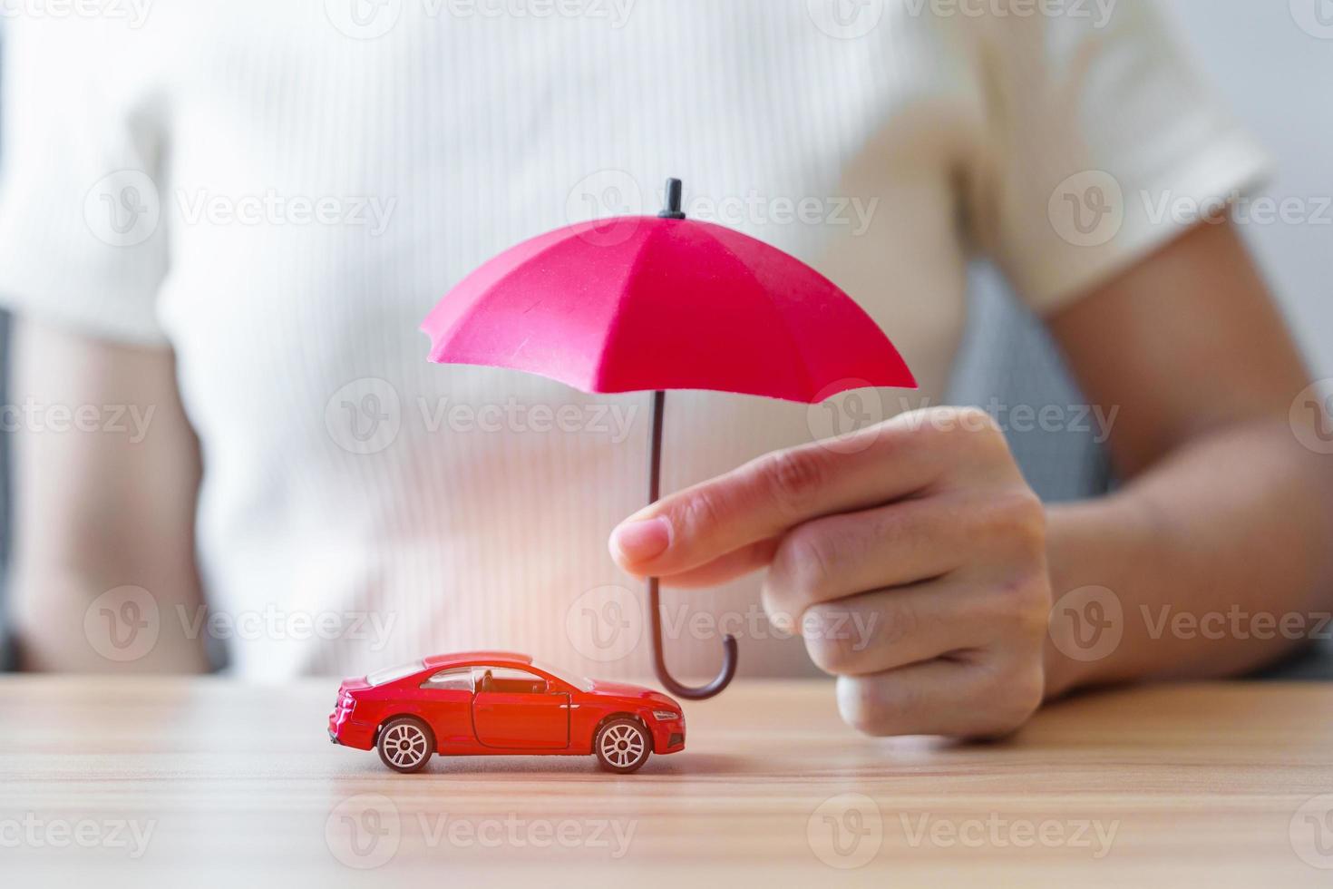 affärskvinna hand innehav röd paraply och omslag röd bil leksak på tabell. bil försäkring, garanti, reparera, finansiell, bank och pengar begrepp foto